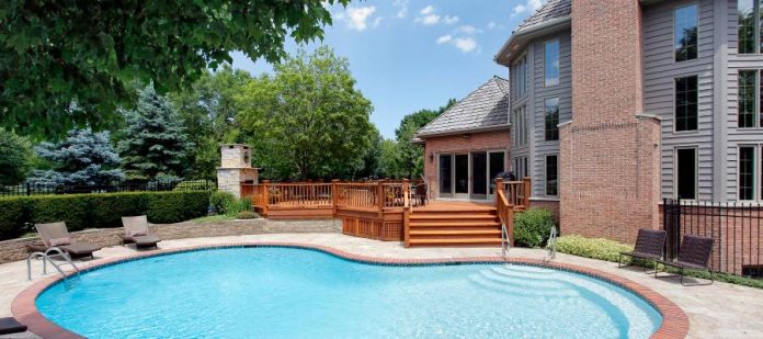 Backyard swimming pool near a home. Two chairs are near the swimming pool, and a wooden deck is in the background.