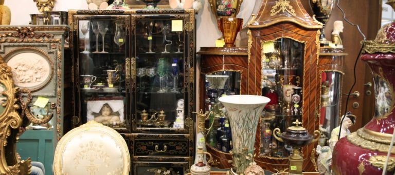 A collection of antiques in a consignment shop. The pieces include China cabinets, vases, wine glasses, and more.