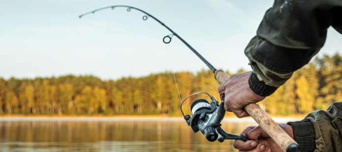 A close-up of a man holding a fishing rod over a body of water. The rod is being pulled down by a fish in the water.