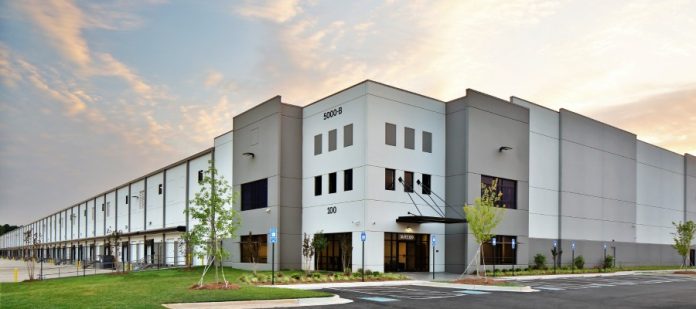 The parking lot and exterior of a white and gray warehouse-type facility at sunrise. The facility is labeled 5000-B.