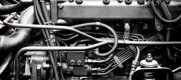 An extreme close-up on a silvery diesel engine is showing the manifold, tubing, pipes, and many other parts.