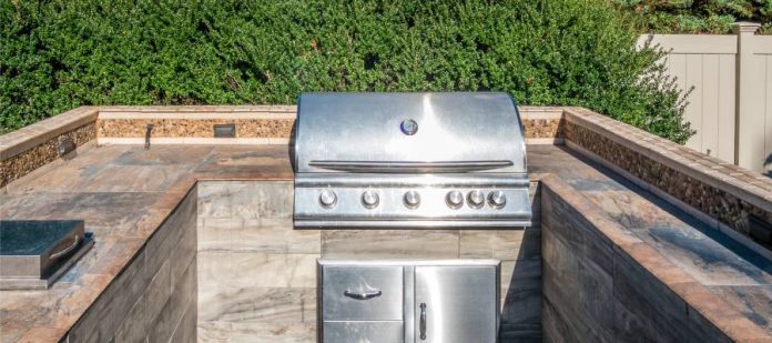 An outdoor kitchen in a residential backyard. Fixated in the counter space is a sterling silver grill.