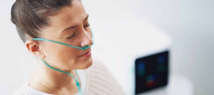 A woman with her eyes closed in a doctor's office, breathing deeply from her oxygen therapy device, which is in her nostrils.