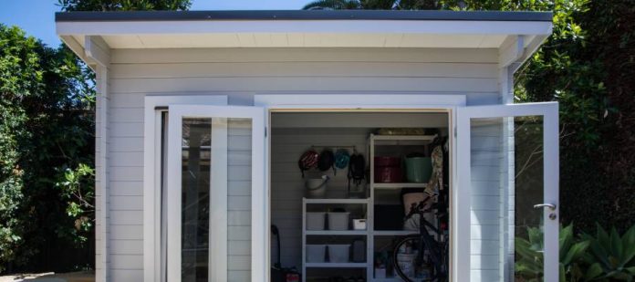 An outdoor shed with a single concrete step and two glass doors that are open to reveal organized storage.