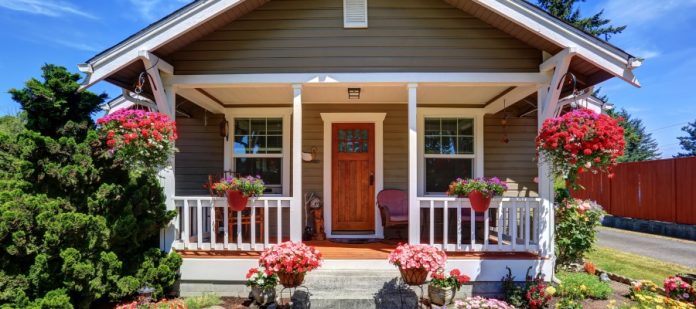 A cute front porch with white railing and a wooden door. There are florals all around the porch area.