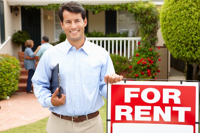 A smiling man holding a clipboard stands next to a 