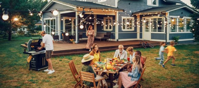 A family spending time outside together. Most of them are gathered around a table, but there are a few off doing other things.