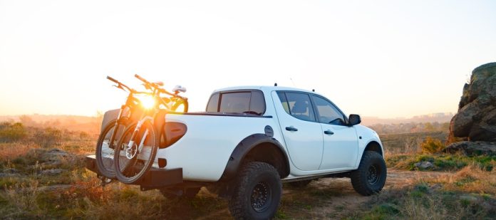 A white pickup truck is parked in the grass during a sunrise. There are two bicycles mounted to the back of the vehicle.