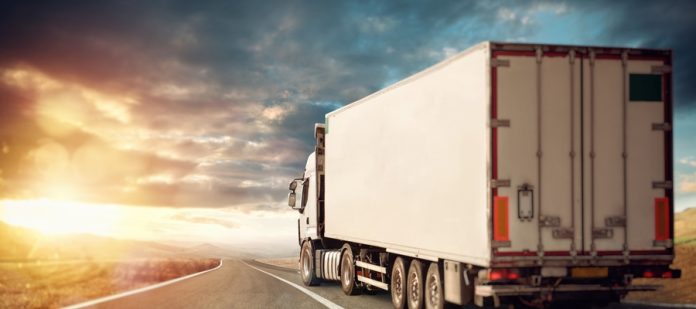 A large white moving van driving along an open road. It's headed toward a sunset happening in the west.