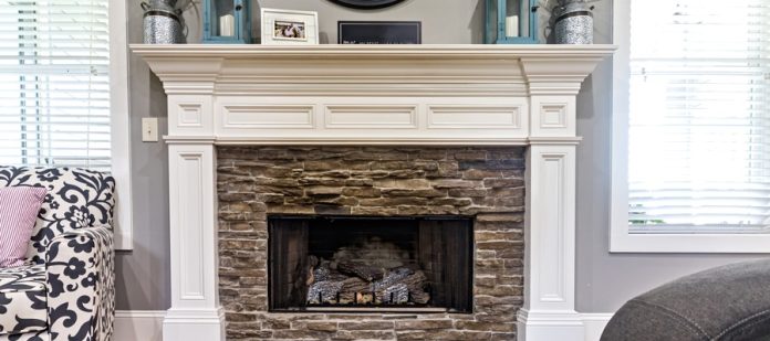 A brick fireplace framed by white painted wood, with plants, turquoise lanterns, and a picture frame on the mantel.