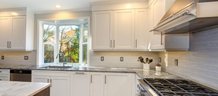 A modern kitchen with an island in the middle. The entire kitchen features white Shaker cabinets with silver hardware.