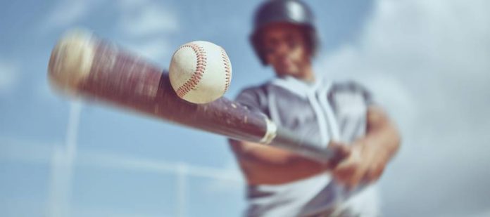 A male baseball player in full gaming gear is swinging and hitting a baseball with the bat very fast.