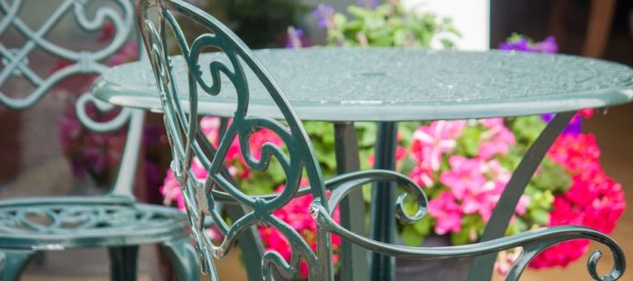 A set of metal bistro chairs and an ornate table painted green. The closest green chair has signs of wear on the back.