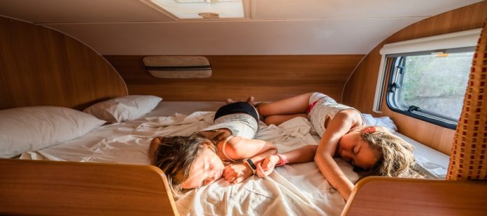 Two young girls sleep on a bed in a motorhome. Sunlight shines through the window.