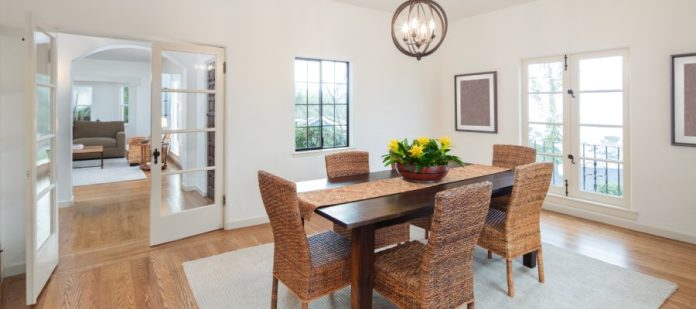 A dining room with a wooden table and wicker chairs. A glass door connects the dining room to the living room.
