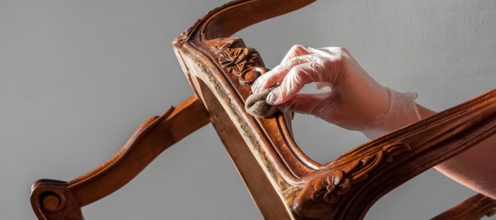 Signs Your Wood Furniture Is Ready for Restoration A person re-staining a solid wood chair with intricate, antique detailing. The stain color is dark cherry.