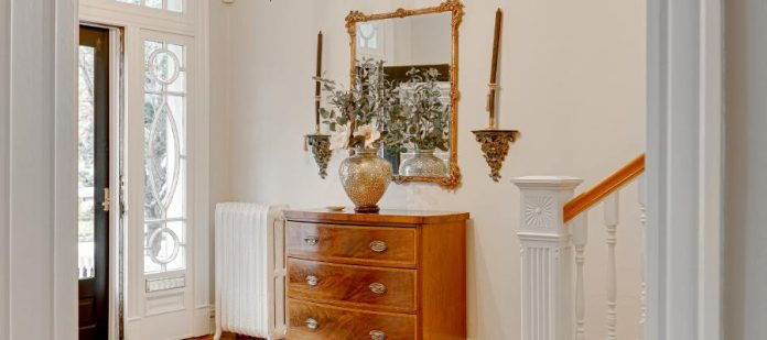A home entryway featuring a wooden chest of drawers, a gold mirror, a decorative vase, and a colorful rug.