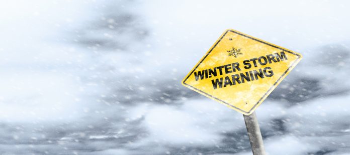 Snow falls heavily around a yellow road sign that reads 'WINTER STORM WARNING