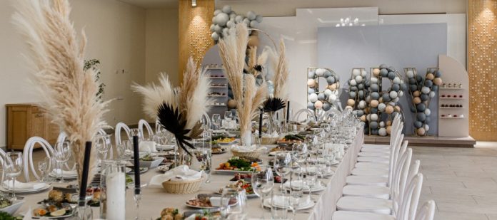 A table decorated with tableware and plants for an event. Balloons at the back of the room are arranged to spell “Baby.”