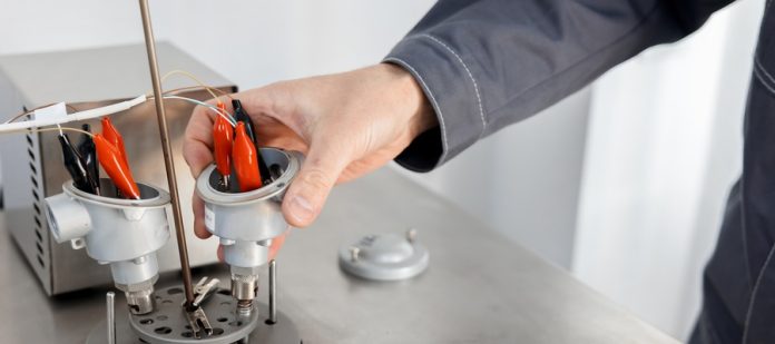 A professional HVAC tech stands at the furnace system of a home as they fidget with the thermocouple component.