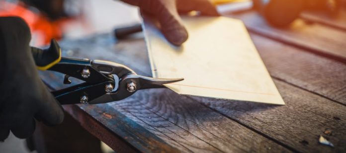 A close-up of someone using a pair of Kevlar shears to trim a piece of work material. They're wearing gloves.