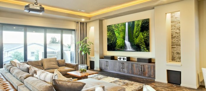 A modern home theater room features leather sofas, wall lights, marble flooring, and a large projection screen.