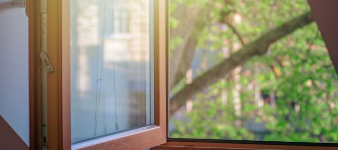 an open wooden window with glass panes and a latch above a wooden sill beside green tree branches outside.