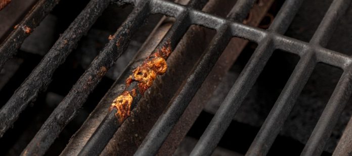 A stainless-steel grill with a piece of burnt food stuck to a grate, with the rest of the grates covered in grease.