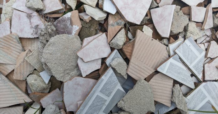Pile of broken ceramic tiles and concrete rubble in varied pink, gray, beige, and white pieces scattered together.