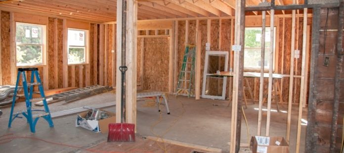 The interior of a home addition under construction with bare floors, exposed studs, and various equipment.